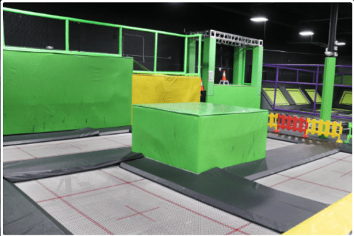 A vibrant indoor trampoline park featuring green and yellow trampolines and safety barriers.