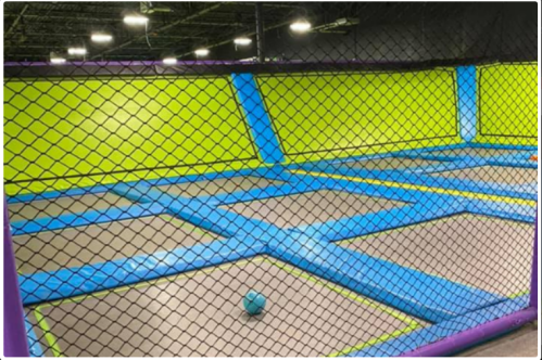 A brightly colored indoor trampoline park with blue and green sections, featuring a single blue ball on the floor.