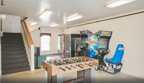 A game room featuring a foosball table, arcade machines, vending machines, and a staircase.