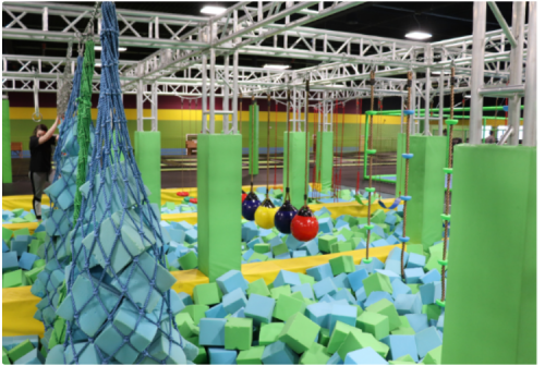 A colorful indoor playground with foam pits, climbing structures, and hanging obstacles for active play.