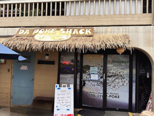 Exterior of Da Poke Shack, featuring a thatched roof sign and a menu board outside, located in Kailua-Kona, Hawaii.