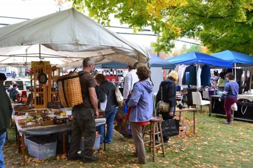 A bustling outdoor market with vendors under tents, showcasing various goods and shoppers browsing among colorful displays.