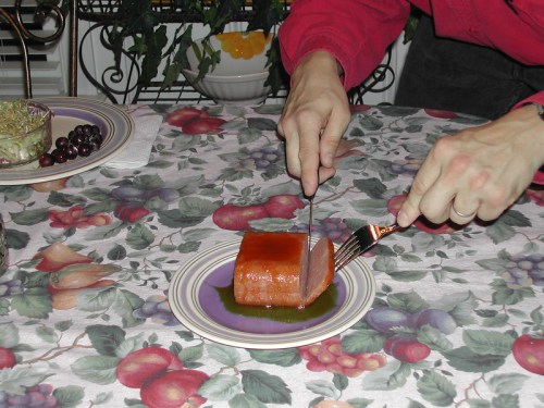 A person cuts into a rectangular piece of food on a plate, with a salad and grapes on the table.