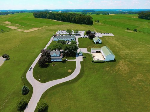 Aerial view of a rural property featuring buildings, parking, and expansive green fields in the background.