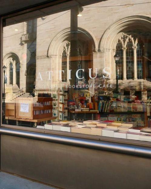 A bookstore café window displays books and a sign, with a historic building in the background.