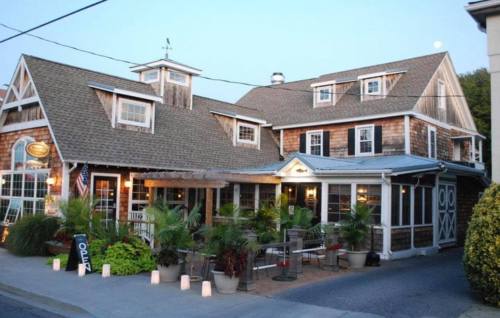 A charming restaurant with a wooden exterior, outdoor seating, and decorative plants, illuminated at dusk.