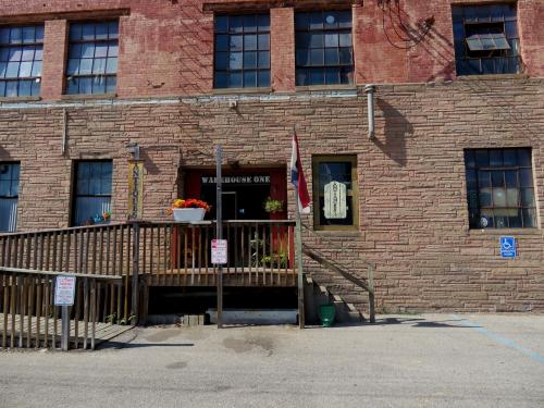 Entrance to Warehouse One, featuring a wooden ramp, potted plants, and a brick building with large windows.