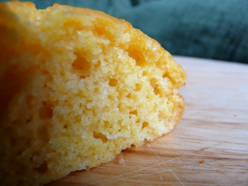 Close-up of a slice of cornbread, showcasing its fluffy, yellow texture and crumb structure on a wooden surface.