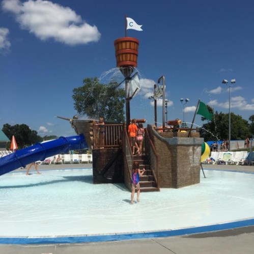 A water play area with a large slide, splash features, and children enjoying the sunny day in a shallow pool.