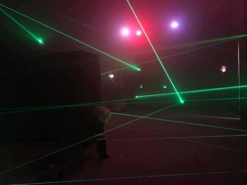 A dimly lit room with green laser beams crisscrossing, creating a maze-like effect.