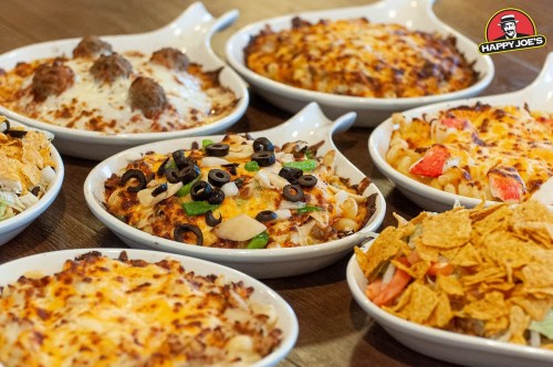 A variety of cheesy, baked pasta dishes in white bowls, topped with vegetables, meats, and olives on a wooden table.
