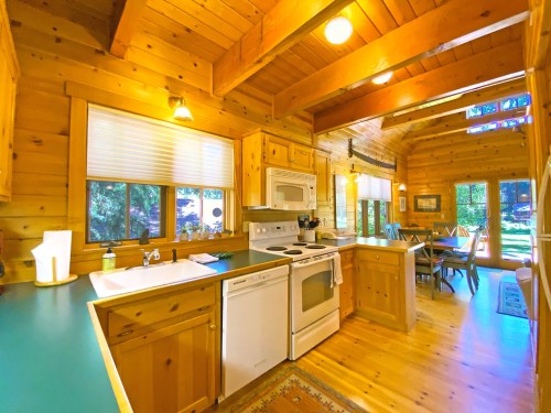 Cozy wooden kitchen with appliances, a dining area, and large windows letting in natural light.