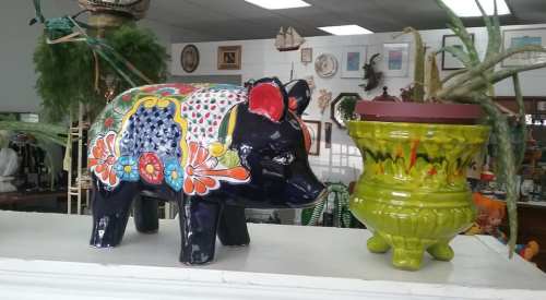 A colorful ceramic pig figurine next to a vibrant green plant pot, displayed in a vintage shop.