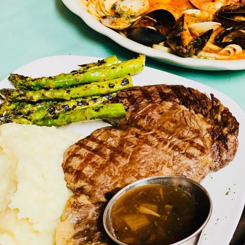 A plate featuring grilled asparagus, mashed potatoes, a steak, and a small bowl of sauce.