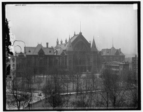 Historic black-and-white photo of a grand, ornate building surrounded by bare trees and a foggy atmosphere.