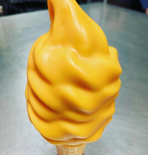 A close-up of a soft-serve ice cream cone with a smooth, bright orange swirl on top.
