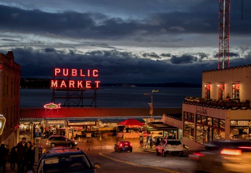A vibrant public market at dusk, with neon lights and bustling activity near the waterfront.
