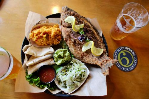 A plate with a whole fried fish, rice, tortillas, guacamole, salsa, and coleslaw, alongside a pint of beer.