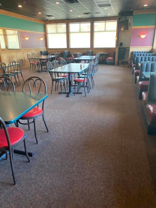 Empty restaurant interior with tables and chairs, carpeted floor, and colorful walls. Natural light from windows.