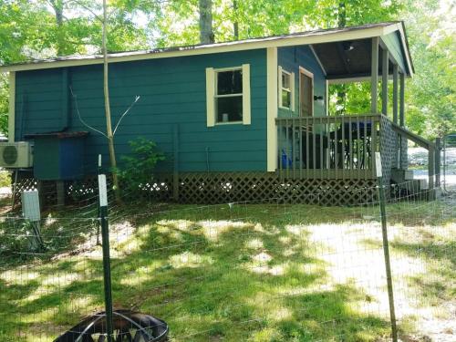 A small blue house with a porch, surrounded by trees and a fenced yard, on a sunny day.