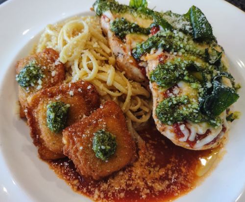A plate of chicken topped with pesto, served with pasta and crispy ravioli in marinara sauce.