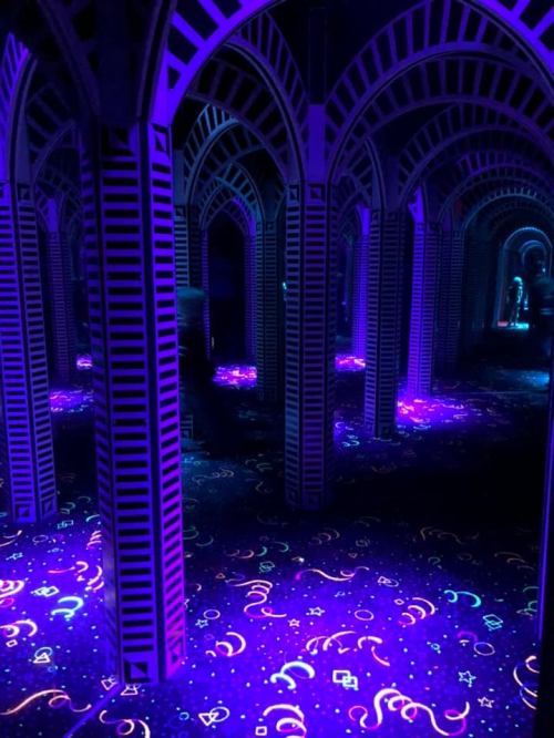 A vibrant, mirrored room with glowing purple arches and a colorful, illuminated floor design.