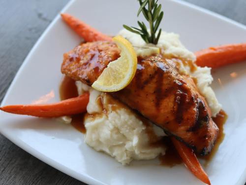 Grilled salmon fillet with lemon, served on mashed potatoes and garnished with carrots and rosemary.