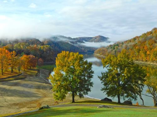 A serene lake surrounded by colorful autumn trees and misty mountains under a cloudy sky.