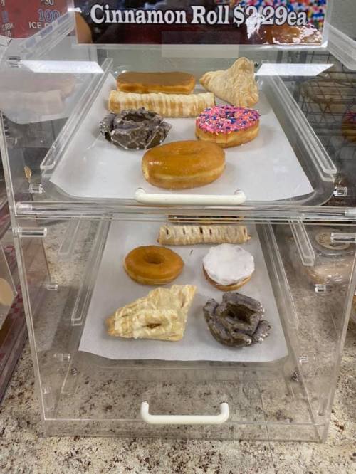 Display case with assorted pastries, including donuts, cinnamon rolls, and cream-filled treats on parchment paper.