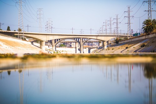 A serene view of a river reflecting a bridge and power lines under a clear blue sky.