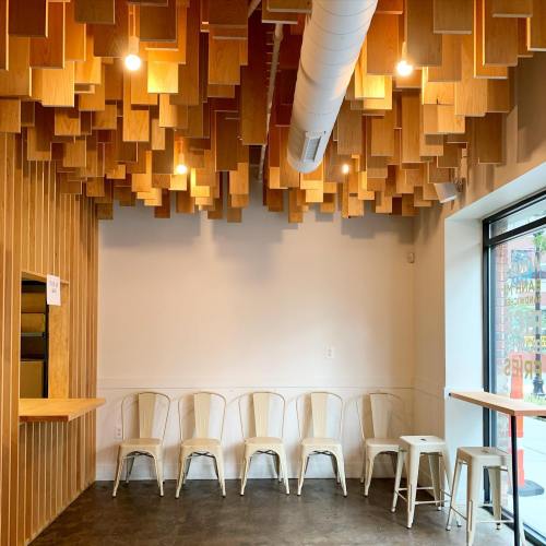 A modern cafe interior featuring wooden ceiling panels, white walls, and metal chairs arranged in a row.