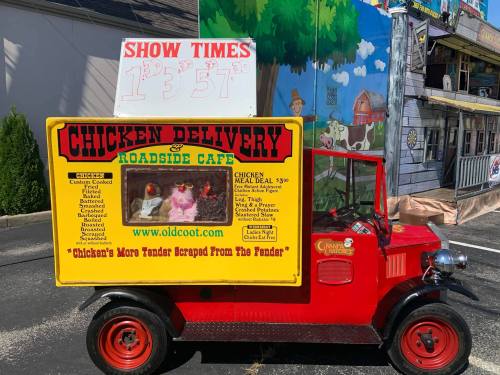 A colorful food truck with a chicken delivery theme, featuring a sign with show times and a playful design.