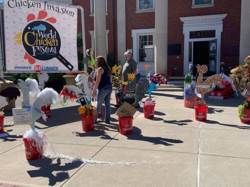 People admire colorful chicken-themed decorations at the World Chicken Festival, with various art pieces displayed in buckets.
