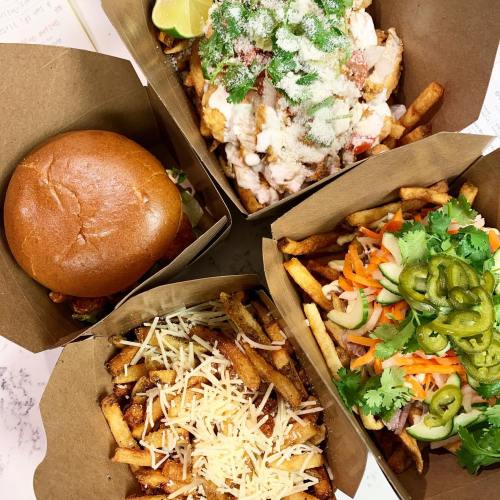 Four takeout boxes featuring fries topped with cheese, a burger, and a chicken dish with toppings and lime.