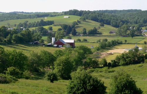 A scenic view of rolling green hills with a red barn and trees in a rural landscape.