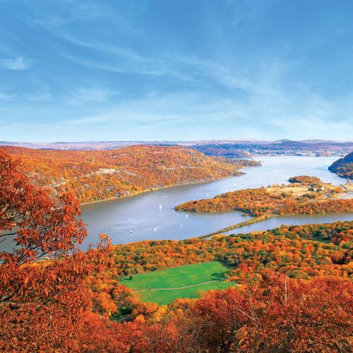 A scenic view of a river surrounded by vibrant autumn foliage and rolling hills under a clear blue sky.