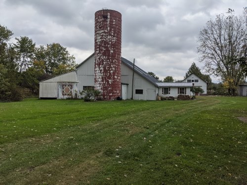 A rustic farm scene featuring a red silo, a white barn, and a grassy area under a cloudy sky.