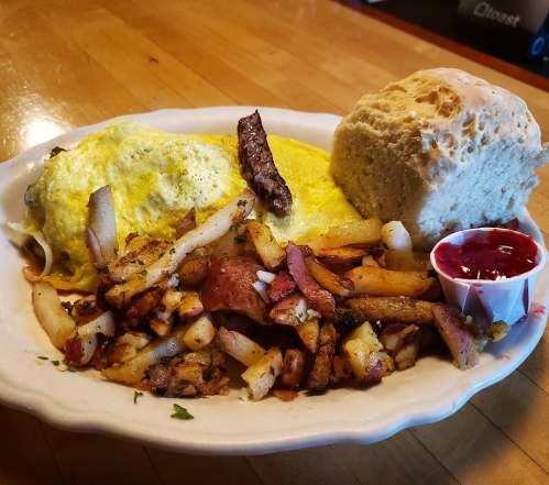 A plate of fluffy omelette, seasoned potatoes, a biscuit, and a small cup of jam.