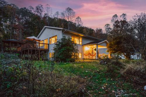 A cozy house with glowing windows, surrounded by trees and a colorful sunset sky.