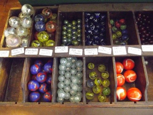 A wooden display with various colorful marbles organized in compartments, each labeled with names and prices.