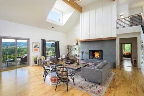 A modern living room with a high ceiling, large windows, a fireplace, and stylish furniture overlooking a scenic view.