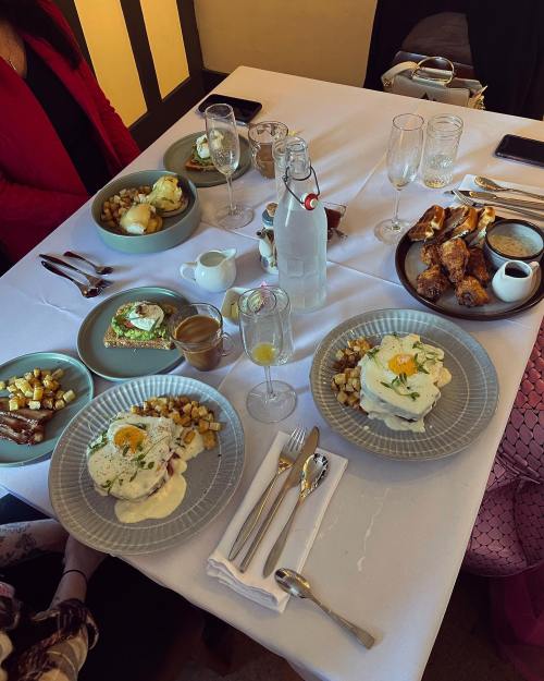 A table set for brunch with plates of eggs, potatoes, pastries, and drinks, surrounded by elegant tableware.