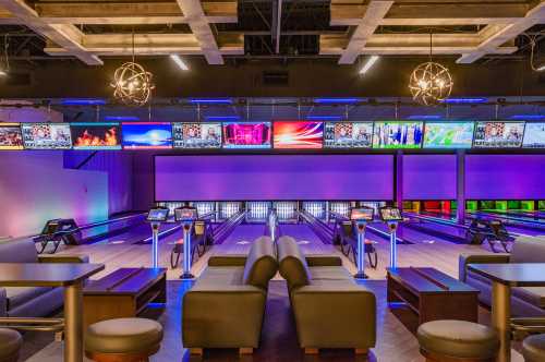 Modern bowling alley interior with vibrant lighting, multiple screens, and comfortable seating areas.