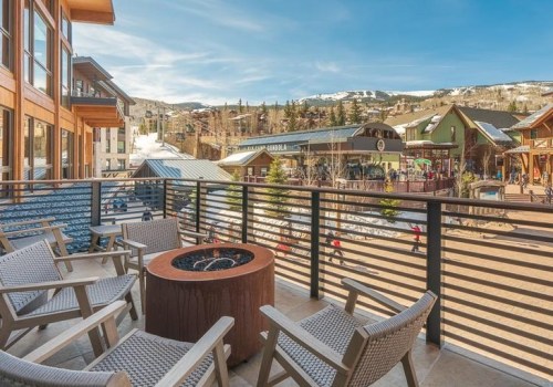 A balcony with seating and a fire pit overlooks a snowy landscape and mountain buildings under a clear blue sky.