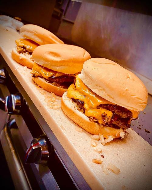 Three cheeseburgers with melted cheese on a grill, resting on a flat surface.