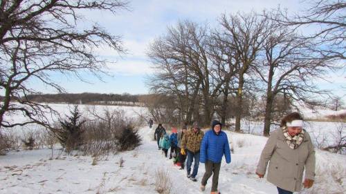 A group of people walking along a snowy path lined with trees on a winter day.