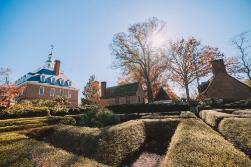 A sunny day at a historic site featuring manicured gardens and colonial-style buildings surrounded by autumn foliage.
