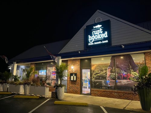 Exterior of a restaurant named "Just Hooked," featuring a bright sign and large windows, at night.
