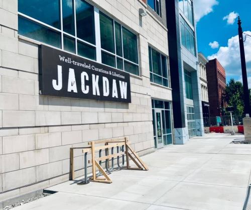 Sign for "JACKDAW" on a modern building exterior, with a bike rack and blue sky in the background.