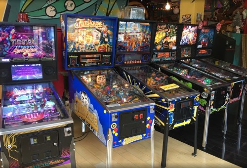 A row of colorful pinball machines in a vibrant arcade setting, featuring various themes and designs.